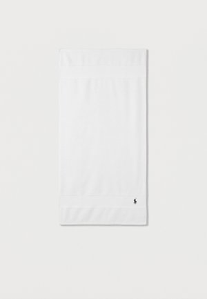 Serviette à main en coton blanc pliée avec un petit logo de cheval sombre brodé dans le coin inférieur sur un fond blanc uni.