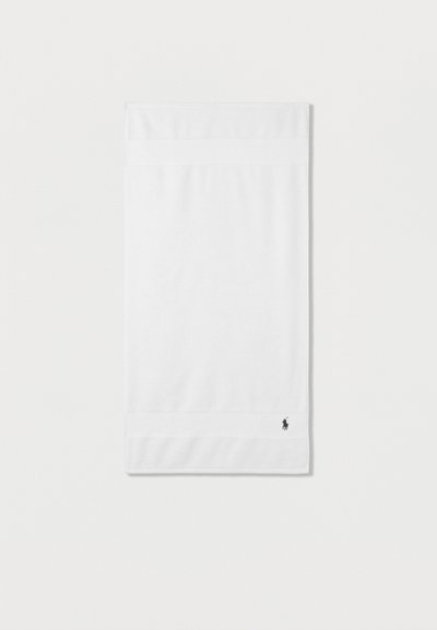 Διπλωμένη λευκή βαμβακερή πετσέτα χεριών με ένα μικρό σκούρο κεντητό λογότυπο αλόγου στην κάτω γωνία σε απλό λευκό φόντο.