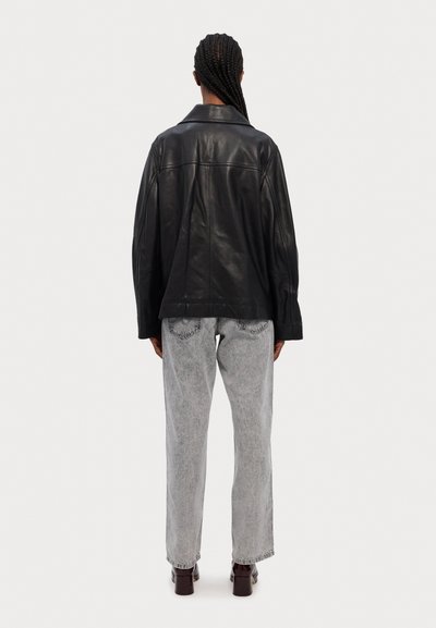 Must must nahktak dževik laia lõike ja laia varrukatega, koos heledate hallide kõrge vöökohtadega teksade ja tumedate kontsakingadega.