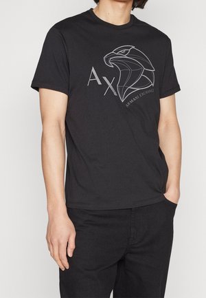 Man wearing black Armani Exchange t-shirt with stylized eagle head graphic and "AX" logo, paired with black pants.