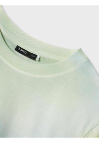 Camiseta de manga corta verde claro con cuello redondo acanalado, que presenta una etiqueta con la marca "LMTD" en negro. Textura de algodón suave.