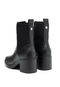 Czarne skórzane botki za kostkę z żeberkowym dzianinowym wierzchem, z zaokrąglonym czubkiem i masywnym słupkowym obcasem. Zawierają metalowy akcent z tyłu.