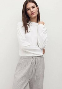 Biała bluzka z długim rękawem i okrągłym dekoltem, zestawiona z jasnoszarymi spodniami w paski, które mają elastyczny pas i sznurek do regulacji.