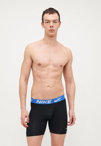Črne Nike boxer gate z modrim vzorčastim pasom, z gladko teksturo in prilegajočo obliko, ki sega do sredine stegna.