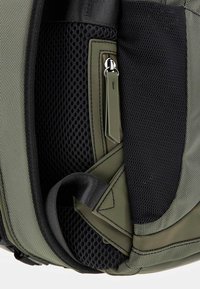 Sac à dos vert olive avec des détails en maille texturée, doté d'une poche zippée et de bretelles réglables. Tissu durable avec des bords renforcés.
