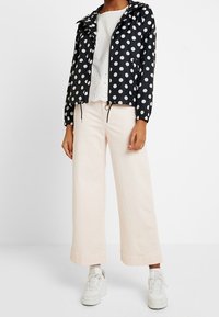 Černobílá větrovka s kapucí s puntíky, doplněná bílým topem a bledě růžovými širokými kalhotami a bílé tenisky pro dokončení vzhledu.