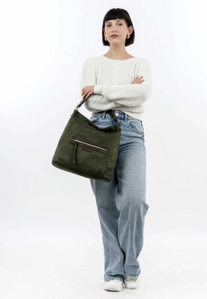 Green suede bag with a zippered front pocket, sturdy strap, and a soft, textured surface. Worn casually with jeans and a knit sweater.