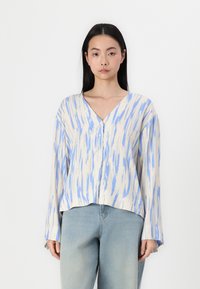 Leichte, V-Ausschnitt-Bluse mit blau-creamfarbigem abstraktem Muster, langen Ärmeln und Knopfdetails am Ausschnitt. Getragen mit hellblauen Jeans.