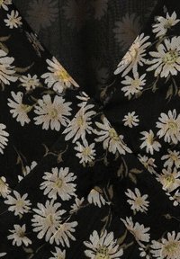 Schwarzer Stoff mit floralem Muster, der weiße Gänseblümchen und grüne Akzente zeigt. Die Textur wirkt leicht und weich, mit einem fließenden Design.