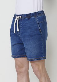 Zili džinsu īsi šorti ar elastīgu jostu, baltu auklu, sānu kabatām un kontrastējošiem šuvju izšuvumiem apakšmalā.