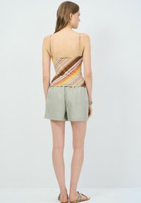 Stribet tanktop i orange, brun og gul med tynde stropper, parret med lysegrønne shorts. Blødt stof, afslappet design.