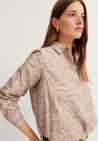 Beige long-sleeve shirt with a white leaf pattern, collared design, and button closure, featuring slightly gathered sleeves and a relaxed fit.