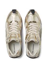 Baskets de sport or et crème avec accents métalliques, panneaux en maille et lacets blancs ; semelle en caoutchouc noir avec motif de texture.