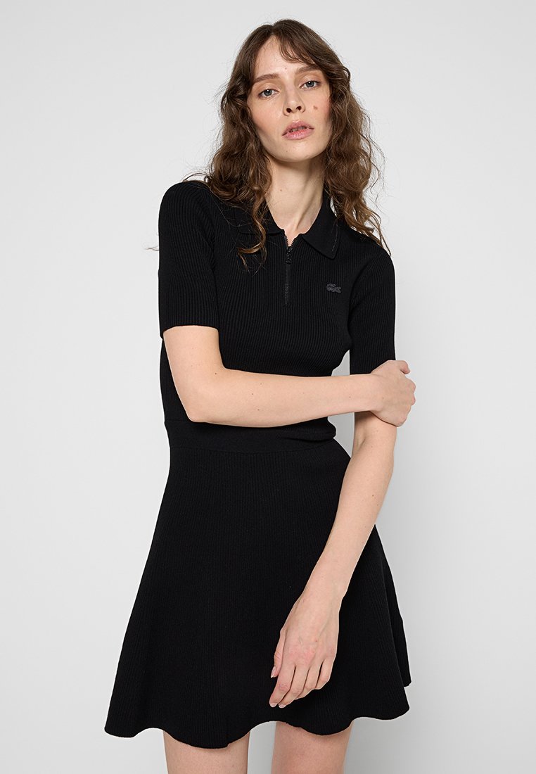 Robe polo noire côtelée avec des manches courtes, un zip mi-haut à l'avant et une jupe évasée. Accent logo discret sur la poitrine. Texture douce.