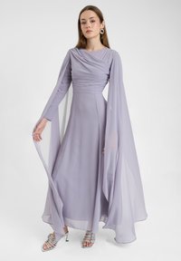 Lange lavendelkleurige jurk met gedrapeerde stof, lange mouwen en een vloeiende silhoeet. Heeft zilveren strappy hakken en een gladde textuur.