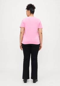 Rosa kortermet t-skjorte med rund hals som er kombinert med flagrende svarte bukser, sett fra bak. Glatt stofftekstur. Ingen mønstre.