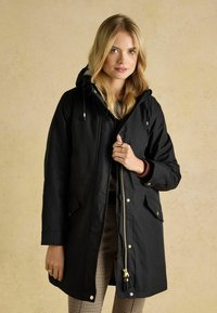 Schwarze wasserdichte Parka mit einem Reißverschluss vorne, Kapuze und zwei Vorderaschen. Ausgestattet mit goldfarbenen Hardwareelementen und einem lässigen, geraden Schnitt.