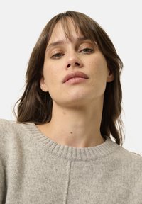 Maglione grigio chiaro con collo a coste e una finitura testurizzata, presenta un taglio dritto e dettagli delle cuciture sottili.