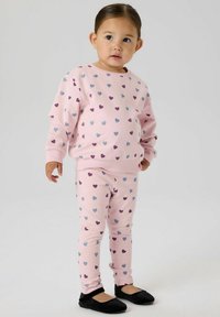 Completo con felpa rosa e leggings con piccoli motivi a cuore viola e blu, realizzato in tessuto morbido. Scarpe basse nere completano l'outfit.