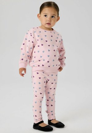 Różowy komplet bluza i legginsy z małymi fioletowymi i niebieskimi wzorami serc, wykonany z miękkiej tkaniny. Do kompletu czarne baleriny.