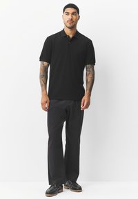 Must must polo särk lühikeste varrukatega, nööbitava kraega, valmistatud siledast kangast. Kombineeritud mustade pükste ja mustade kingadega, minimalistlik disain.