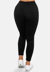 Leggings de mezclilla negra con un diseño ajustado, que cuentan con bolsillos traseros y una cintura de altura media. Textura suave con un ligero estiramiento. Llevados con zapatillas blancas.