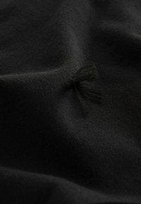 Tissu noir avec un petit détail texturé en boucle ou pompon créant de légers plis et ombres sur la surface douce du matériau.