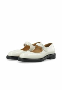 Zapatos Mary Jane de charol blanco con puntera redondeada, una única correa ajustable con hebilla y suela de goma negra. Presentan un detalle de superficie texturizada.