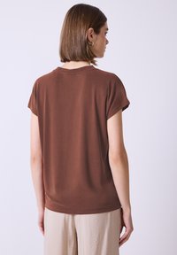 Hnědý top s krátkým rukávem a volným střihem, kulatým výstřihem, vyrobený z hladké tkaniny. Zadní pohled ukazuje minimální detaily švů.