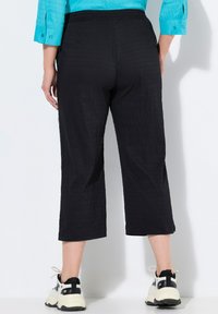 Zwarte, cropped broek van textuurstof, met een wijde poot ontwerp en elastische tailleband, gecombineerd met zwart-witte sneakers.