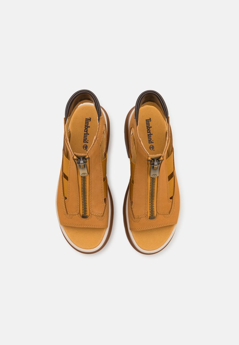 Braune Leder-Sandalen mit einem Reißverschluss, offenen Zehen und Ausschnitten an den Seiten. Die Sohle ist weiß mit einem braunen Akzent. Timberland-Logo sichtbar.