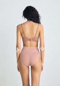 Haut de bikini rose avec des bretelles réglables et un fermoir à crochets, associé à un bas taille haute. Tissu lisse, design minimal.