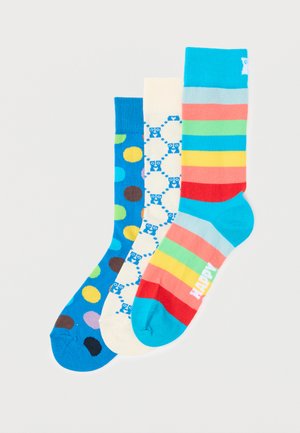 Three colorful mid-calf socks side by side: blue with large multicolor dots, cream with blue sheep pattern, and rainbow stripes with "HAPPY" text.
