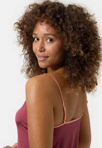 Top sans manches bordeaux avec des bretelles fines ajustables, présentant une texture lisse et un léger éclat. Le mannequin a des cheveux bouclés, atteignant les épaules.