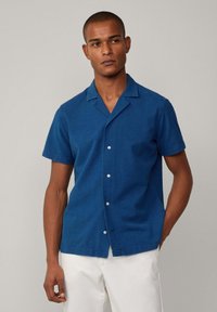 Blauwe kortarm overhemd van textuurstof, met een notch-kraag en witte knopen, gecombineerd met witte broek.