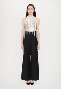 Top cu guler halter de culoare metalică argintie, cu franjuri, asociat cu pantaloni largi negri cu talie înaltă și pantofi cu toc ascuțit negri.