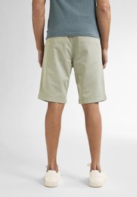 Shorts din bumbac verde deschis cu o croială lejeră, până la genunchi, cu buzunare laterale și tiv cusut, asortați cu adidași albi.