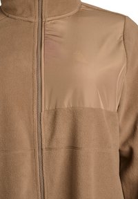 Braune Fleecejacke mit einem glatten Stoffeinsatz auf der oberen Brust. Verfügt über einen mittigen Reißverschluss und dezente Markenkennzeichnung auf dem strukturierten Stoff.