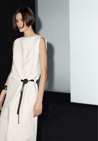 White sleeveless linen dress with a fitted waist and black fabric belt. Smooth texture, relaxed fit, minimalistic design, and subtle draping.
