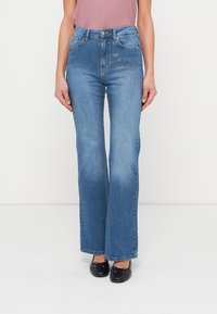 Μπλε τζιν με καμπάνες από denim, με μεσαία μέση, πέντε τσέπες και διακοσμητικές λεπτομέρειες στο μπροστινό μέρος.