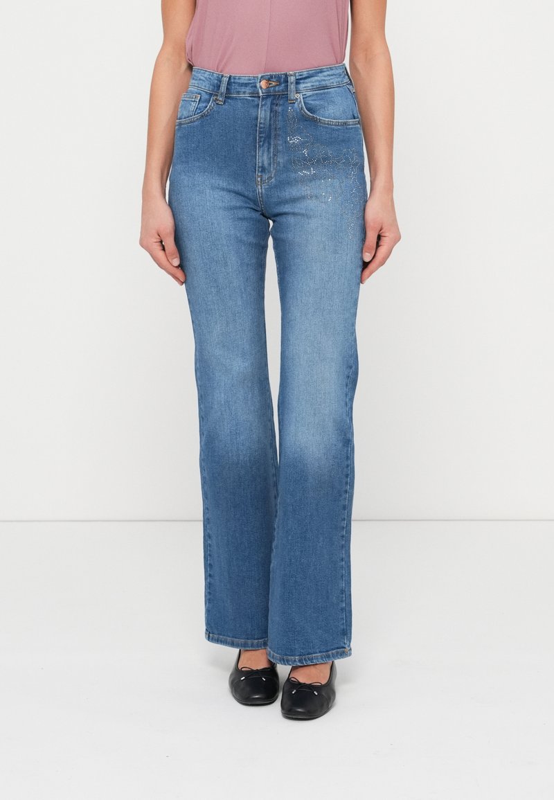 Μπλε τζιν με καμπάνες από denim, με μεσαία μέση, πέντε τσέπες και διακοσμητικές λεπτομέρειες στο μπροστινό μέρος.