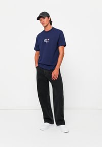 Navy blue T-shirt with white "USA" text and flag graphic, paired with black loose-fit jeans and white sneakers, accented by a gray cap.