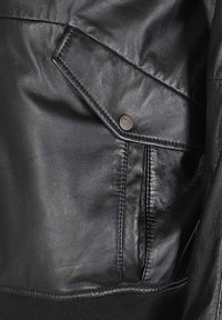 Zwarte leren jas met een gestructureerde afwerking, diagonale zak met een metalen drukknoop en geribde manchetten aan de onderkant.