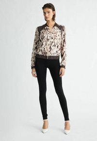 Chaqueta bomber de estampado de leopardo en tejido ligero, con un cuello y puños oscuros, combinada con leggings negros y tacones blancos de punta.