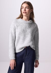 Grau, flauschiger Strickpullover mit hohem Ausschnitt und langen Ärmeln, kombiniert mit dunkelblauen Jeans. Subtile Textur und lässige Passform.