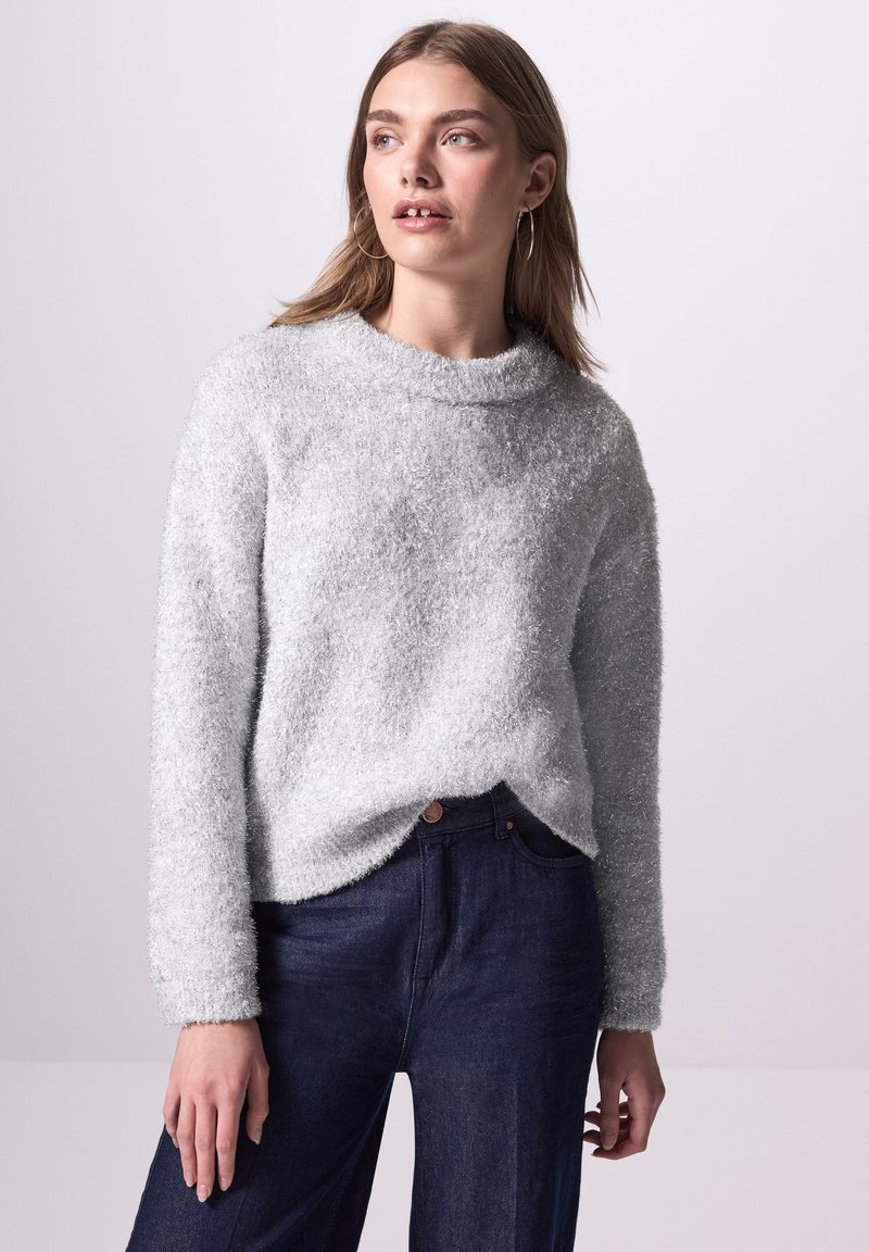Grau, flauschiger Strickpullover mit hohem Ausschnitt und langen Ärmeln, kombiniert mit dunkelblauen Jeans. Subtile Textur und lässige Passform.