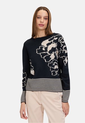 Marineblauwe trui met grote witte bloemenpatronen aan één kant, afgewerkt met een gestreepte zoom. Gemaakt van een zachte, gestructureerde breiwijze.