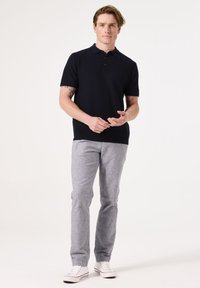 Marineblauw polo-shirt met korte mouwen en een gestructureerd brei-design, gecombineerd met lichtgrijze broek en witte sneakers, staand tegen een effen achtergrond.