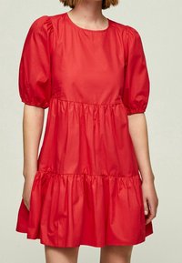Vestido de algodón rojo con mangas cortas abullonadas, escote redondo y dobladillo de volantes en capas. Textura suave, material ligero. Diseño sencillo.