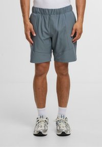 Světle modré sportovní kraťasy s elastickým pasem, s bočními kapsami a prošitým detailem, doplněné šedými teniskami a bílými ponožkami.